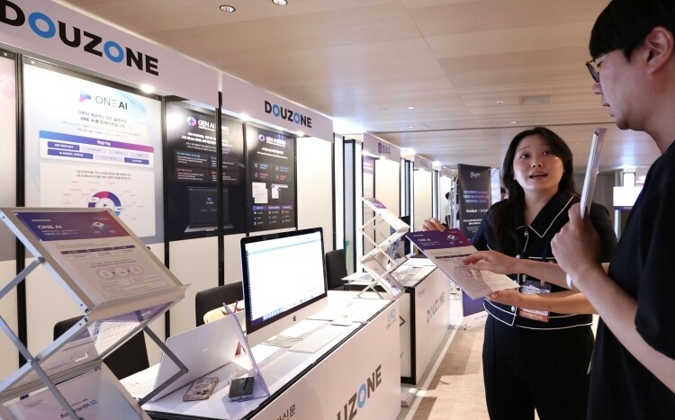 CAIO Summit 2026 행사장에 마련된 더존비즈온 전시 부스에서 참관객이 ‘ONE AI’와 ‘GEN AI DEWS’를 살펴보고 있다.
